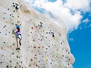 Asian athletic woman practicing rock climbing on a rock wall, outdoor activity with blue sky background, low angle view.