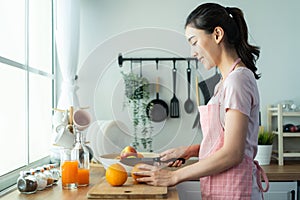 Asian attractive woman make drinking orange juice in kitchen at home. Smiling young beautiful girl wear apron feel happy enjoy