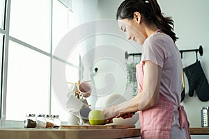 Asian attractive woman make drinking orange juice in kitchen at home. Smiling young beautiful girl wear apron feel happy enjoy
