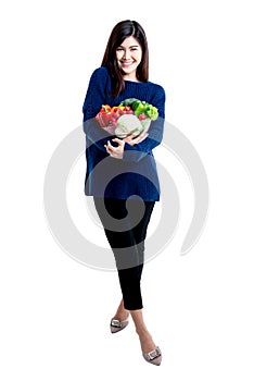Asian attractive woman, standing and holding a bowl containing fresh fruit and vegetables
