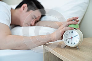 Asian attractive young man turn off alarm clock ringing in the morning. Handsome male feel lazy and tired lying down on