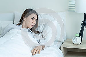 Asian attractive young woman feel shock after wake up late in bedroom. Beautiful girl in pajamas look at alarm clock and awake