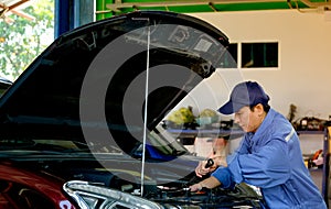 Asian automotive mechanic with blue uniform use wrench to fix the problem in part of engine around bonnet and front bumper of car