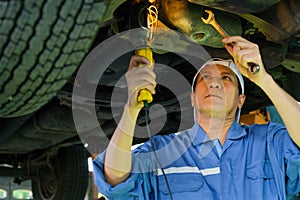 Asian automotive mechanic with blue uniform use wrench to fix the problem under the car in the garage
