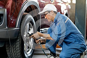 Asian automotive mechanic with white cap and blue uniform is working with replace or fix the problem of car wheel in the garage