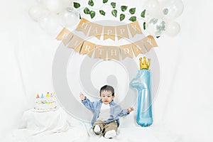 Asian baby boy celebrating first birthday,Cake for 1 year.Infant, small cute child dressed in t-shirt and blue shirt sitting on th