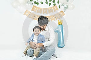 Asian baby boy celebrating first birthday,A father sits and hug his son smiling on a floor with a minimal background,white