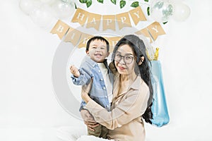 Asian baby boy celebrating first birthday,A mother sits and hug her son smiling on a floor with a minimal background,white