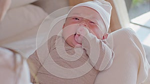 Asian baby boy is laying on mom`s lap, enjoying Motherhood. Son seems so sleepy and moody, trying to bite his hand. The cute