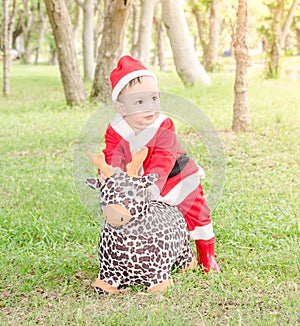Asian baby boy in santa claus suit is ridding reindeer doll