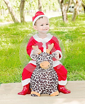 Asian baby boy in santa claus suit is ridding reindeer doll