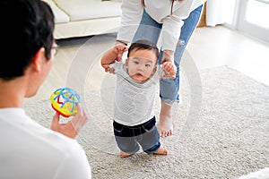 Asian baby boy toddler taking first steps. Family of father and mother encouraging their son learning to walk