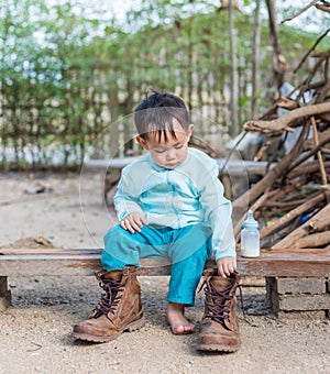 Asian baby boy try to wearing father boots while drinking milk