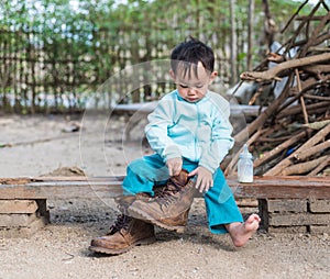 Asian baby boy try to wearing father boots while drinking milk