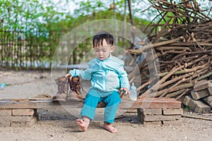 Asian baby boy try to wearing father boots while drinking milk