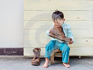 Asian baby boy try to wearing father boots while drinking milk from bottle