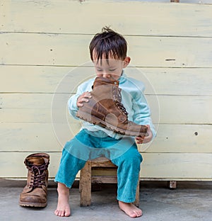 Asian baby boy try to wearing father boots while drinking milk from bottle