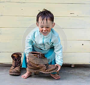 Asian baby boy try to wearing father boots while drinking milk from bottle