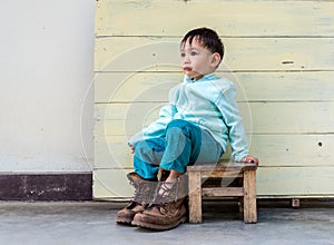 Asian baby boy try to wearing father boots while drinking milk from bottle