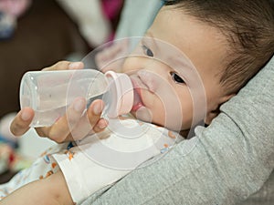Asian baby eating milk in bottle.
