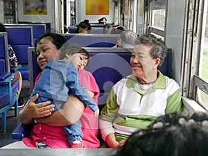 Asian baby girl leaning on her auntie`s shoulder with her grandmother sitting next to during a trip by train photo