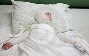 Asian baby girl lying sick with bandaged head and arm on bed at hospital. Baby girl with head and arm injuries.