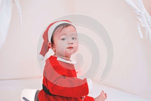 Asian baby girl in a Santa costume. Beautiful little baby celebrates Christmas. Christmas baby.