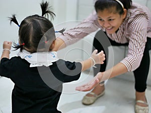 Asian baby girl walking towards her mother, while the mother leaning forward with hands reaching out ready to support her daughter