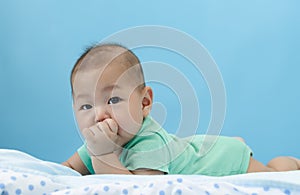 Asian baby laying on bed with his finger in mouth