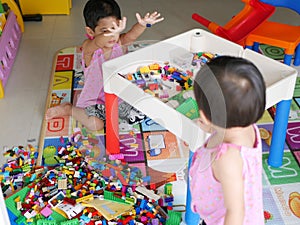 Asian baby left is cleaning up toys she played with her little sister