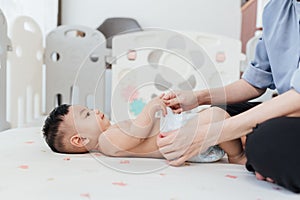 Asian baby shirtless lying on bed is changing diaper by his mother. Baby healthcare hygiene concept