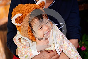 Asian baby smile in mother hugging.Baby girl points her finger at her mouth,she wearing orange cute bear hat with winter cloth