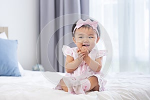 Asian baby toddler in cute pink dress is smiling while sitting on the bed with happiness for healthy kid and adorable girl