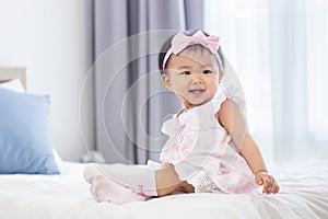 Asian baby toddler in cute pink dress is smiling while sitting on bed with happiness for healthy kid and adorable girl portrait