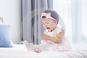 Asian baby toddler in cute pink dress is smiling while sitting on bed with happiness for healthy kid and adorable girl portrait