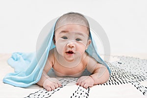 Asian baby under the towel after bathing at home lying on a bed under blue towel,Portrait of a crawling baby