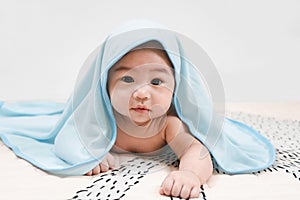 Asian baby under the towel after bathing at home lying on a bed under blue towel,Portrait of a crawling baby