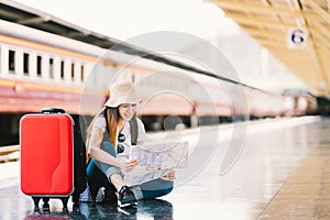 Asian backpack traveler woman using generic local map, siting alone at train station platform with luggage