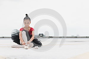 Asian ballerina girl tying pointe shoelace before practicing the ballet dancing sitting on rooftop of the building top view of