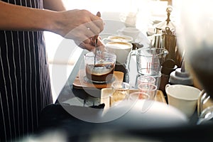 Asian barista young man making coffee according to order at counter bar with natural sunlight in the morning in modern cafe.
