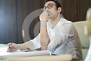 Asian bearded designer sitting, thinking and sketching ideas indoors
