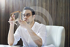 Asian bearded designer sitting, thinking and studying chair model in hand indoors