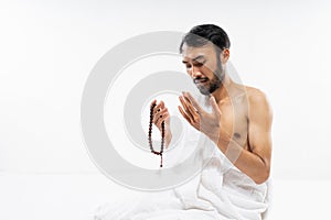 Asian bearded man wearing ihram clothes praying with prayer rug