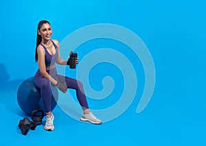 Asian beautiful happy woman holding bottle and sitting on fit ball after exercise isolated on blue background. Woman healthy and