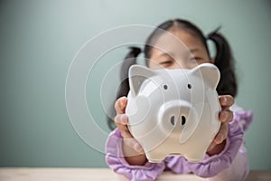 Asian beautiful little cute kid girl holding the white piggy bank with copy space. Savings money for education to the future.