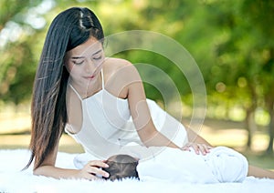 Asian beautiful mother take care her newborn baby who lie on white carpet in the garden