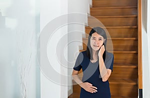 Asian beautiful pregnant woman standing with hand holding her belly at house,Happy mood and positive thinking