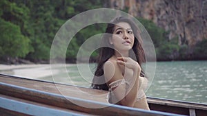 Asian beautiful sensual woman in crochet bikini on the boat. Video of girl sitting on the boat and looking up to the sky in s