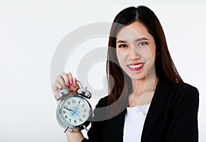 Asian beautiful smiley business woman with long hair wearing formal suit, holding alarm clock and looking to camera with isolated