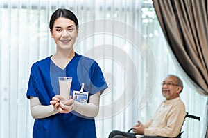 Asian beautiful therapist doctor serve milk to older patient in house. Young woman nurse at nursing home taking care of disabled